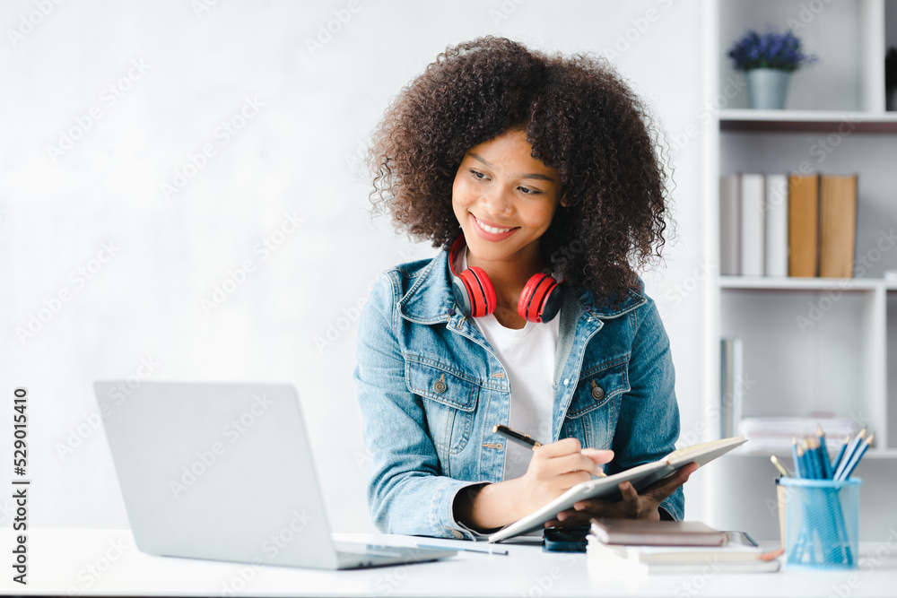 American teenage woman sitting in white office with laptop, she is a student studying online with laptop at home, university student studying online, online web education concept. American teenage woman sitting in white office with laptop, she is a student studying online with laptop at home, university student studying online, online web education concept.