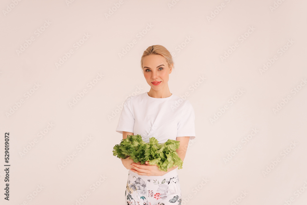 A smiling woman holds a plate of salad and eats celery, the girl is on proper nutrition and on a diet. White isolated background. Nutritionology. Place for text. Copy space A smiling woman holds a plate of salad and eats celery, the girl is on proper nutrition and on a diet. White isolated background. Nutritionology. Place for text. Copy space