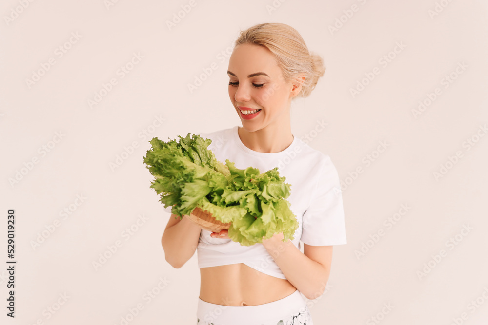 A smiling woman holds a plate of salad and eats celery, the girl is on proper nutrition and on a diet. White isolated background. Nutritionology. Place for text. Copy space A smiling woman holds a plate of salad and eats celery, the girl is on proper nutrition and on a diet. White isolated background. Nutritionology. Place for text. Copy space
