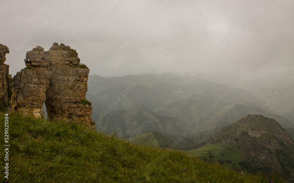 Dramatic landscape - panoramic view of a hilly green valley blurred in a misty haze and steep stone cliffs from the Bermamyt plateau in Karachay-Cherkessia on a cloudy summer day