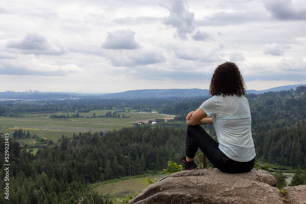 Adventurous Woman Standing on top of a rock overlooking the Canadian Nature Landscape. Minnekhada Regional Park, Coquitlam, Vancouver, British Columbia, Canada.