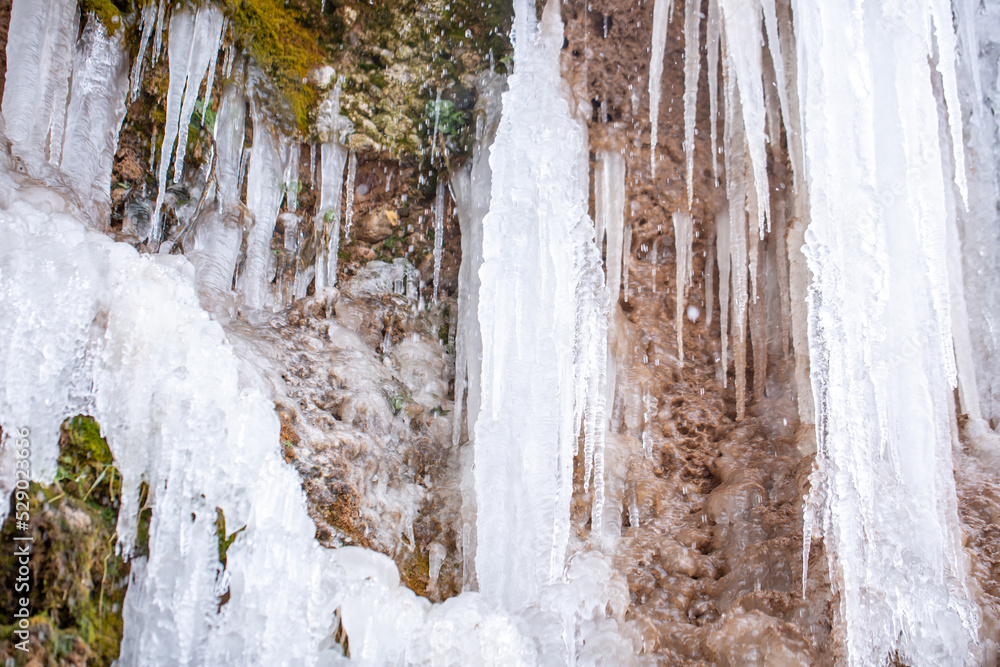 Frozen waterfalls on rocks with icicles in Iceland. Moss in ice. Spring warming, melting ice, dripping water of melted icicles. Frozen waterfalls on rocks with icicles in Iceland. Moss in ice. Spring warming, melting ice, dripping water of melted icicles.