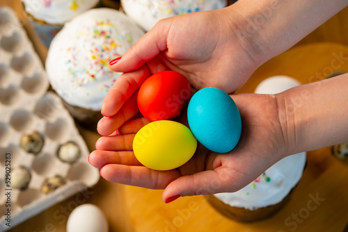 Woman holds Easter colored painted eggs in her hands against background of table with cakes.