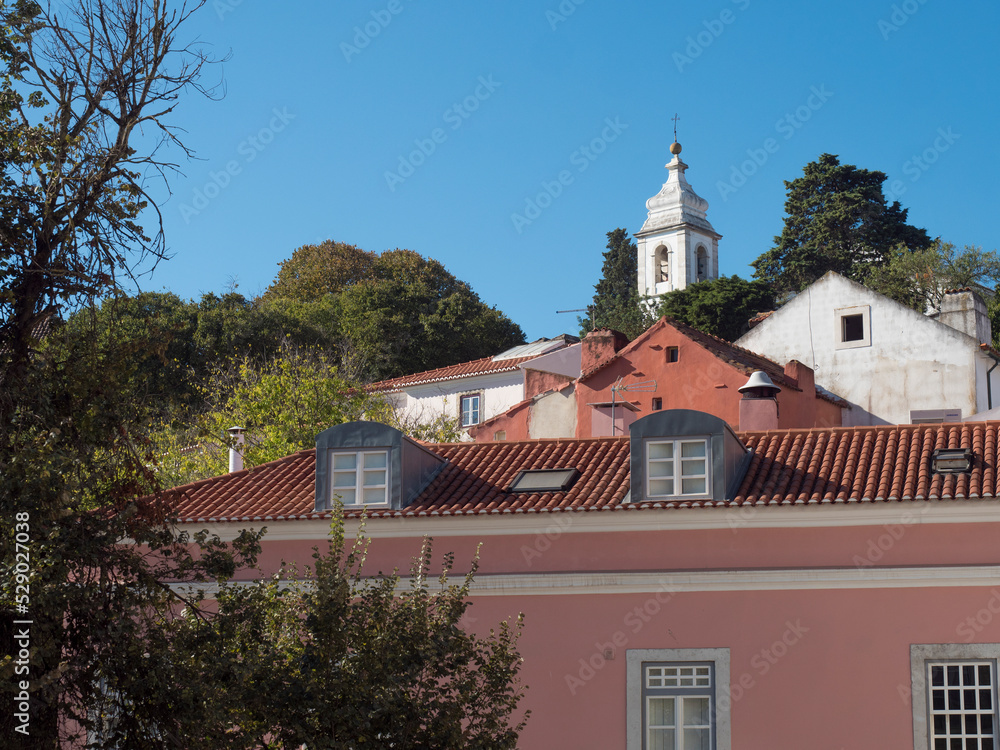 View of pink house and church bell tower at Alfama at Santa Maria Maior district, Lisbon, Portugal. Blue sky background