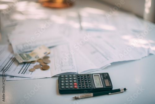 A calculator, some coins and a lot of paper utility bills on the table in close-up. No one. Place for the inscription.