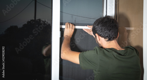 Man installing the mosquito net on the window.