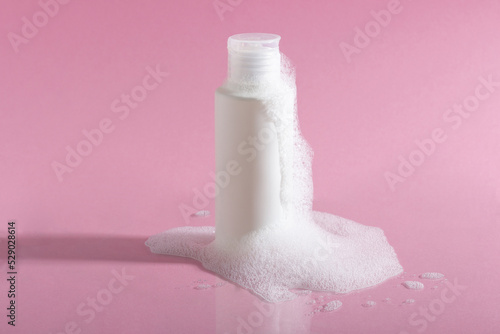 Cosmetics for face, body and hair care. Moisturizer, shampoo or facial cleanser on pink background with foam
