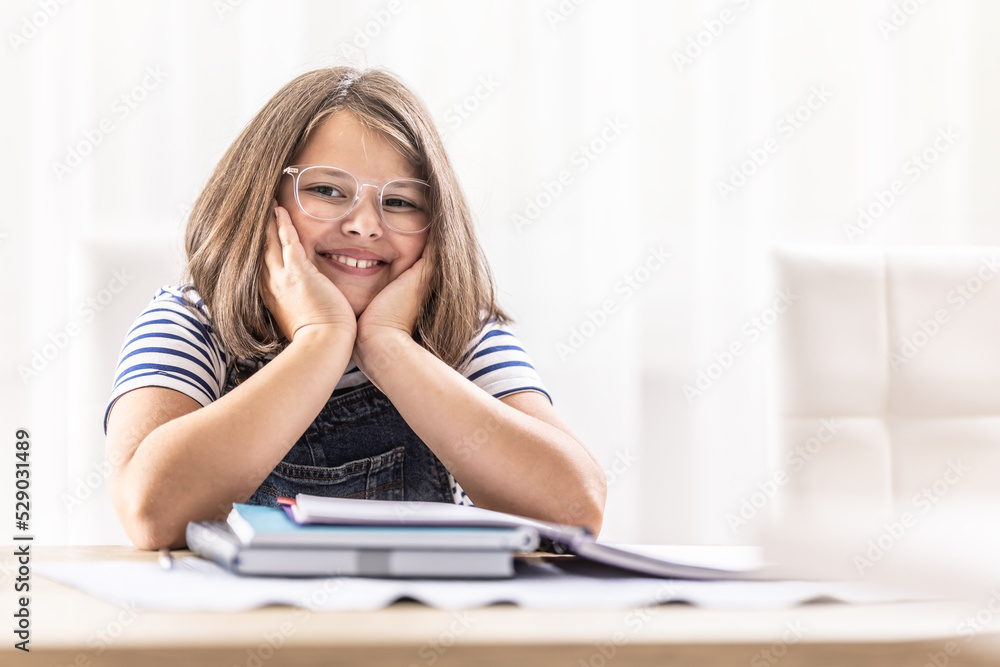 Smiling round-faced girl wearing glasses smiles over pile of school books Smiling round-faced girl wearing glasses smiles over pile of school books