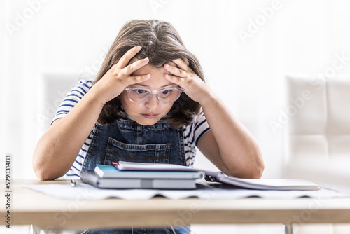 Foto Schoolgirl in glasses tries to comprehend study materials holding her head by bo