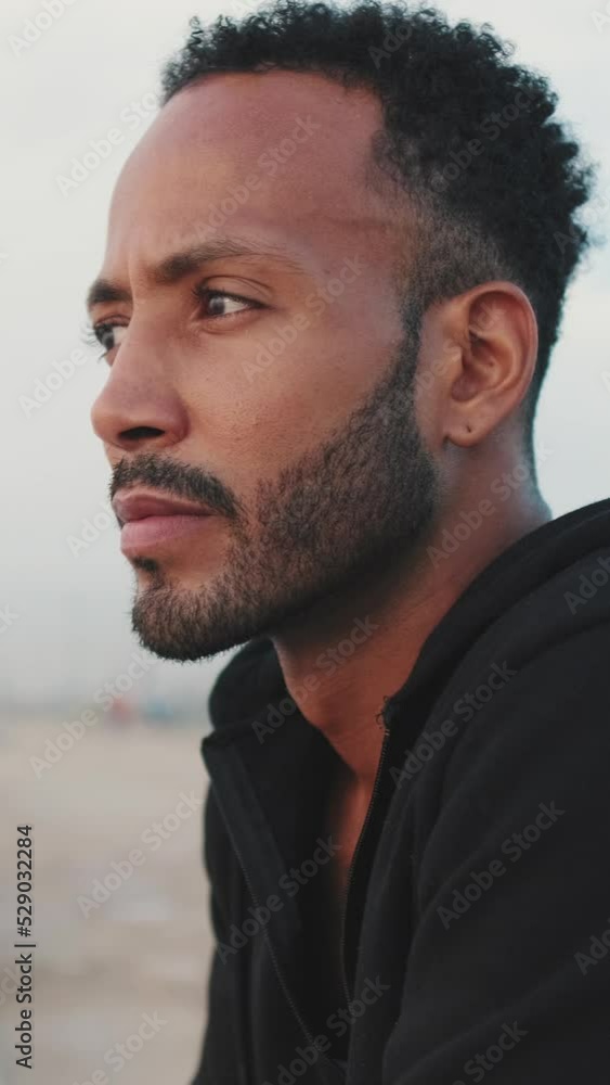 VERTICAL VIDEO: Young bearded male athlete standing on the embankment, looking at the sea. Camera moving forwards VERTICAL VIDEO: Young bearded male athlete standing on the embankment, looking at the sea. Camera moving forwards