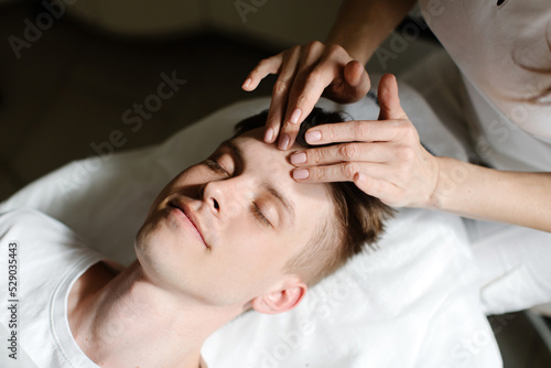 A man lies in a beauty parlor and enjoys a facial massage. Close-up of a man's portrait and woman's hands. High quality photo