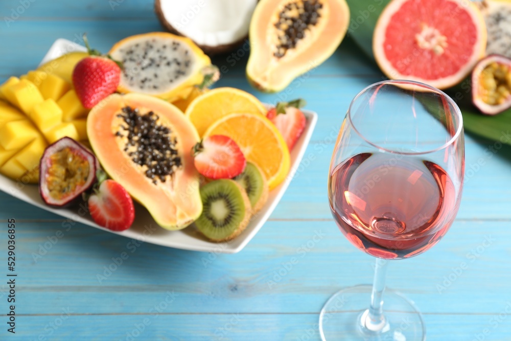Delicious exotic fruits and glass of wine on light blue wooden table Delicious exotic fruits and glass of wine on light blue wooden table