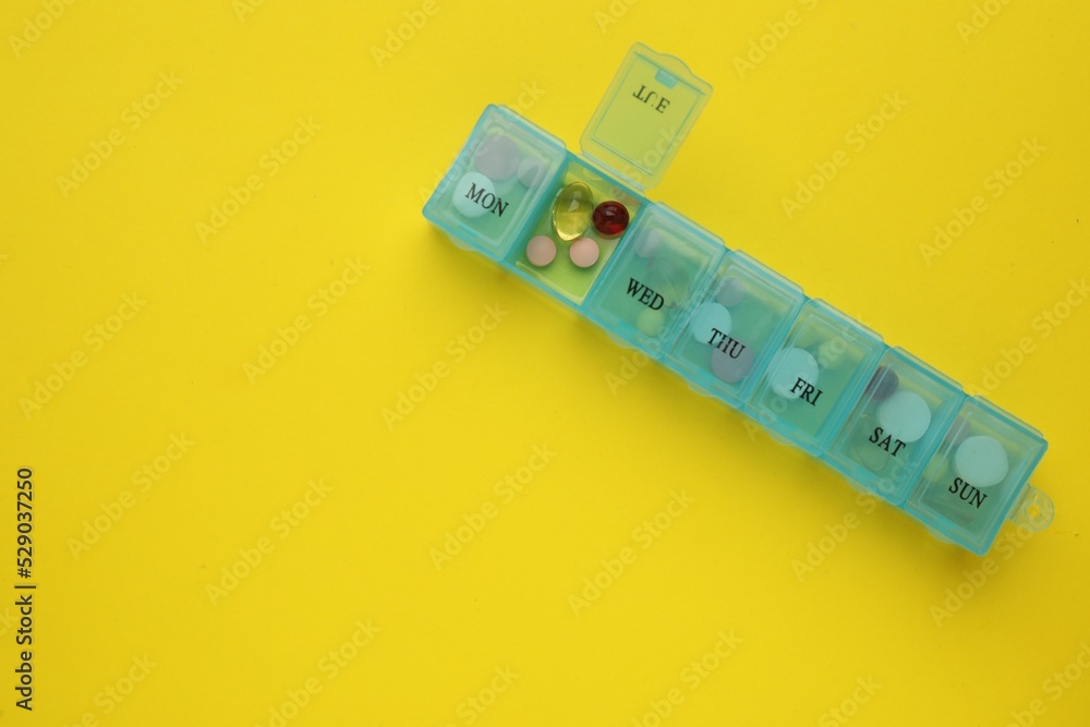 Plastic box with different pills on yellow background, top view. Space for text Plastic box with different pills on yellow background, top view. Space for text
