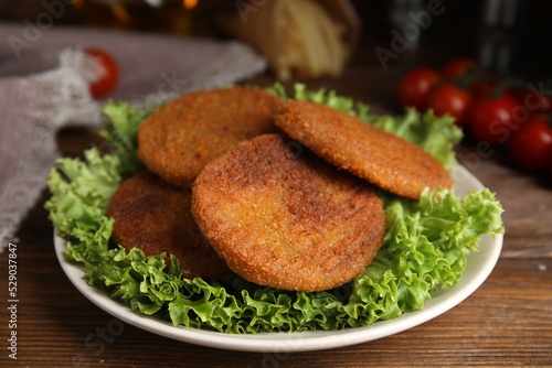 Delicious fried breaded cutlets with lettuce on wooden table, closeup