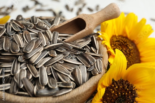 Raw sunflower seeds in bowl and flowers, closeup