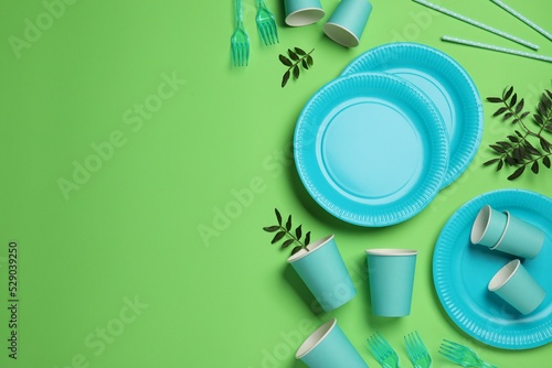 Flat lay composition with disposable tableware on green background, space for text