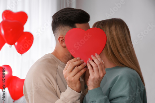 Lovely couple kissing behind decorative heart at home. Valentine's day celebration