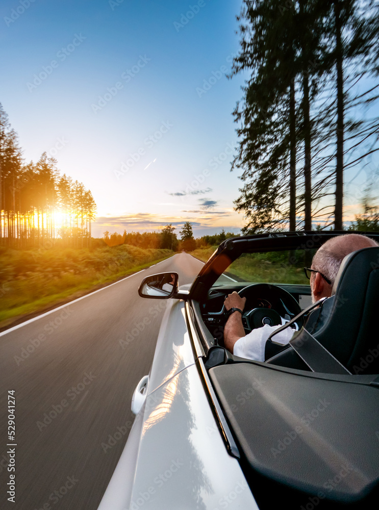 Adult man is driving with convertable car in sunny nature on a bright summer day. wide angle pursuit shot with high speed motion blur. vertical shot