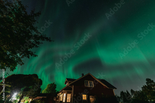 Dancing Northern lights Aurora borealis in autumn over wooden house, garden and garage. Umea town, Sweden, night.