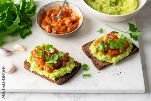 Vegan avocado toast with baked beans and parsley on marble board, closeup view