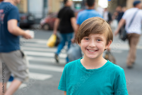 portrait of a happy boy. the child is about to cross the road on a pedestrian crossing or zebra crossing. schoolboy in front of the road and crowds of people crossing the roadway © Ruslan Russland