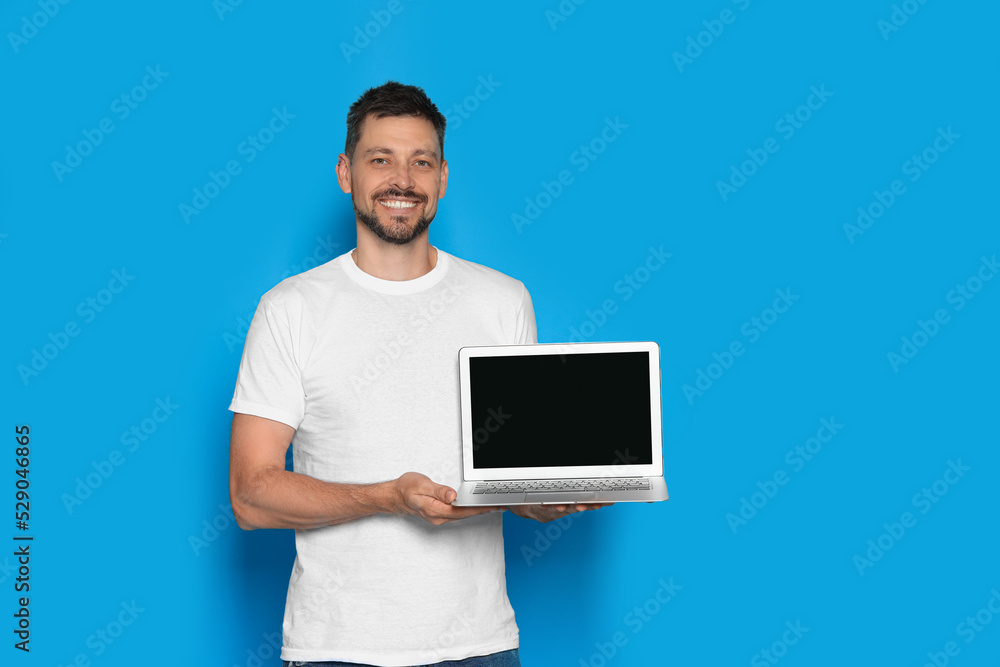Happy man holding laptop on light blue background. Space for text Happy man holding laptop on light blue background. Space for text
