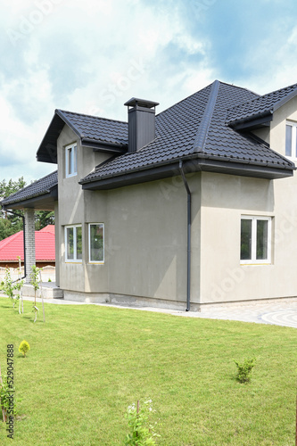 Facade of a concrete private house under a gray roof. The modern house in suburban settlement