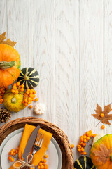 Thanksgiving day concept. Top view vertical photo of rattan basket with plate knife fork napkin pumpkins pattypan pine cone maple leaves rowan on isolated white wooden table background with copyspace