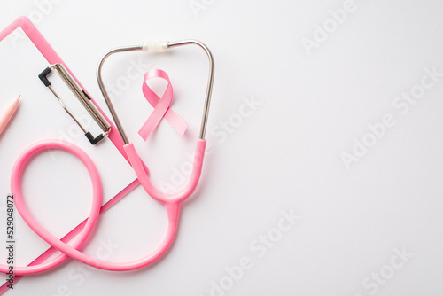 Top view photo of pink ribbon symbol of breast cancer awareness stethoscope pen and clipboard on isolated white background with copyspace