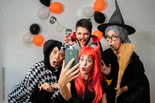 Halloween party at home. Devil, witch, dracula and harlequin making gestures while taking a selfie with their smartphone