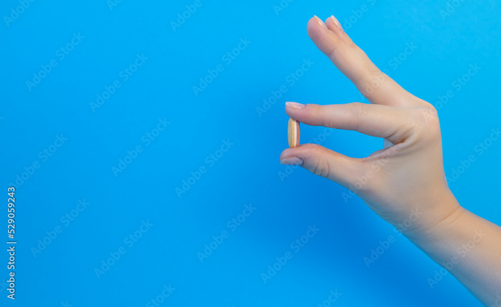 Female hand holding a white pill on a blue background with copy space. The concept of treatment, pharmacy, healthcare