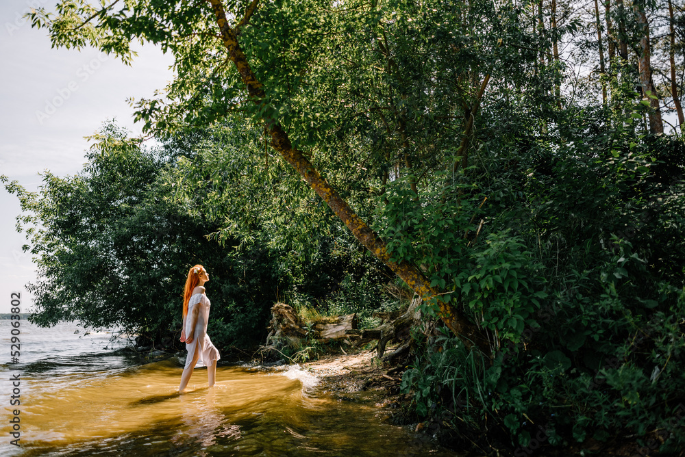 Woman in summer white dress stands on the seashore and looks at the horizon. Young beautiful girl standing in the water Woman in summer white dress stands on the seashore and looks at the horizon. Young beautiful girl standing in the water