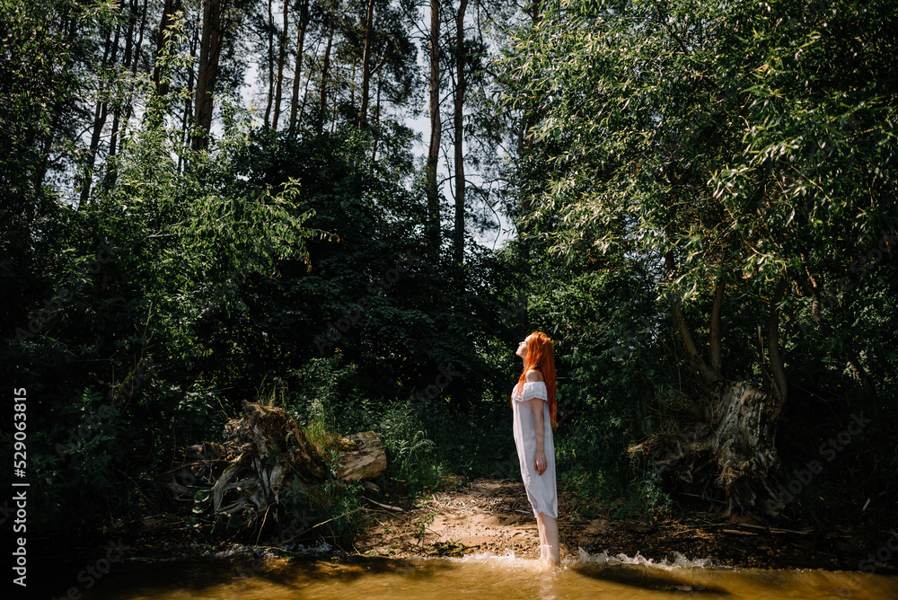 Woman in summer white dress stands on the seashore and looks at the horizon. Young beautiful girl standing in the water