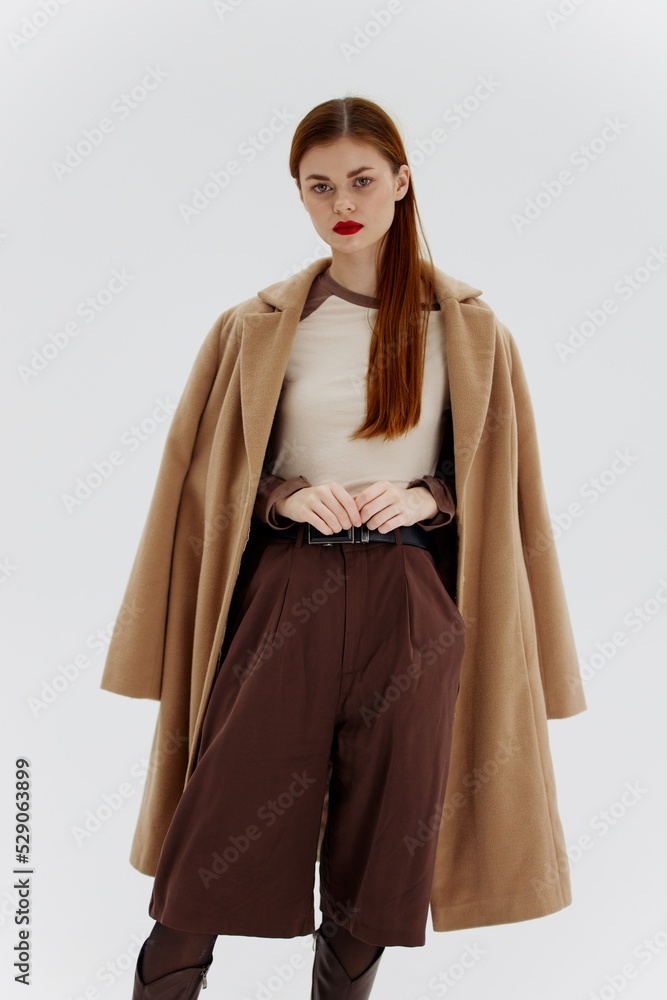 A red-haired lady in a beige coat on a white background. Advertising for brands showrooms catalog of clothing for women