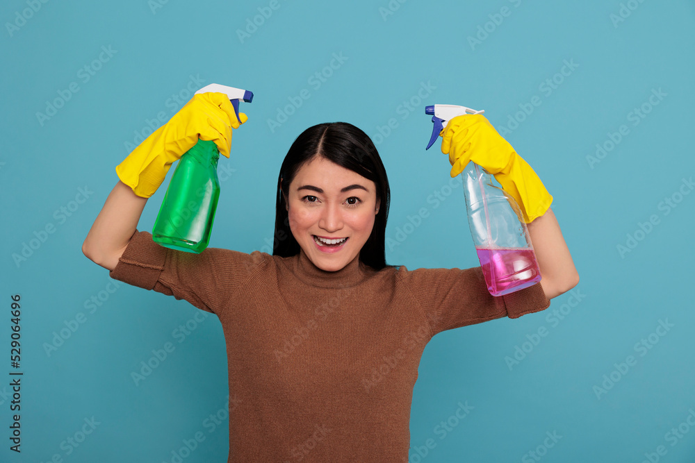 Excited glade and optimistic asian housekeeper at work raising arms holding two detergent sprays in the yellow gloves, Cleaning home concept, Cheerful pleased and positive housewife from chores Excited glade and optimistic asian housekeeper at work raising arms holding two detergent sprays in the yellow gloves, Cleaning home concept, Cheerful pleased and positive housewife from chores