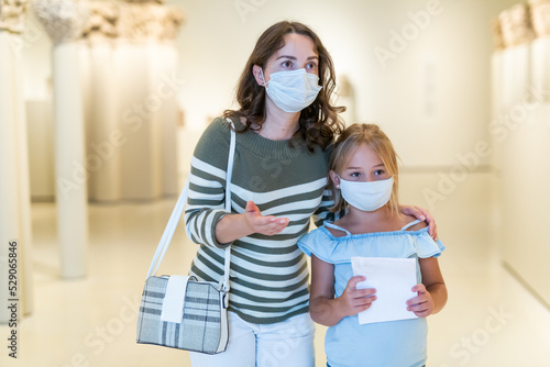 Girl with woman looking with interest at ancient sculptures in museum, using guidebook