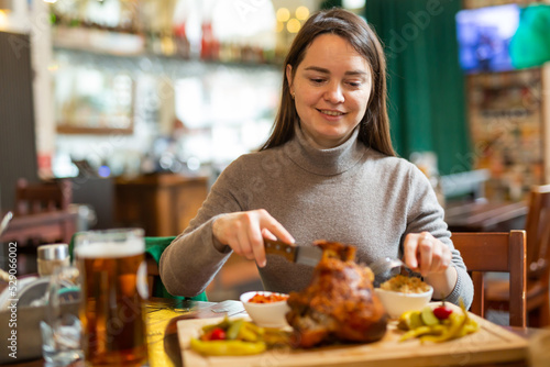 Female traveler tasting fried pork ham knuckle traditionally served with stewed cabbage  pickled vegetables  various sauces and beer in cafe in Vienna. Popular snacks