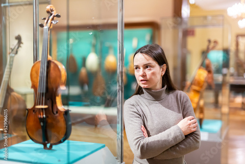 Photography Portrait of interested adult brunette visiting exhibition of medieval musical instruments in historical museum