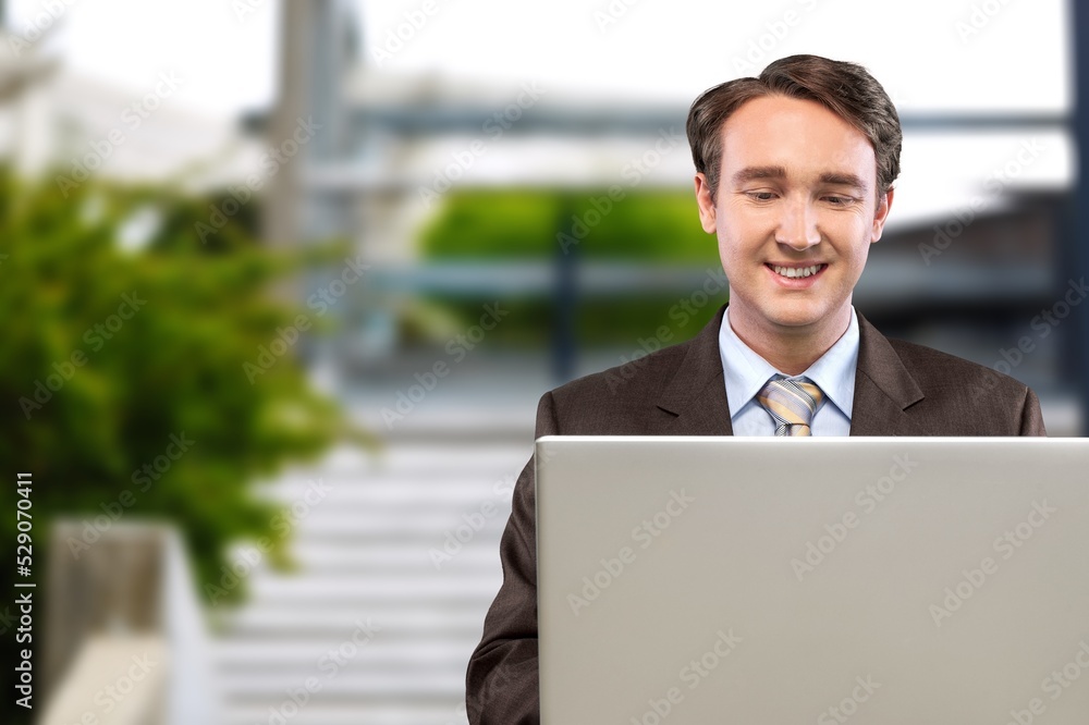 Smiling man sitting outdoors in park and typing on laptop keyboard Smiling man sitting outdoors in park and typing on laptop keyboard