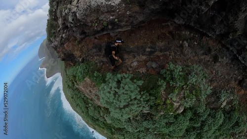 A fit and young man is hiking alone on the narrow path next to the steep edge in Quebrada do Negro in Madeira.