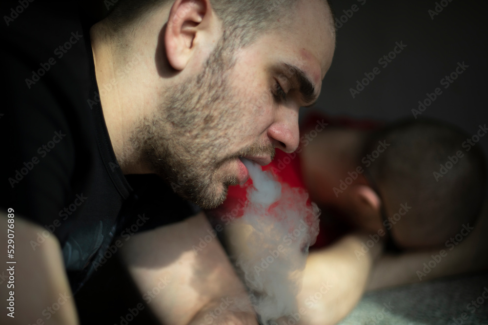 Fototapeta premium Guy smokes. Man with cigarette. Man is tired. Head in sunlight.