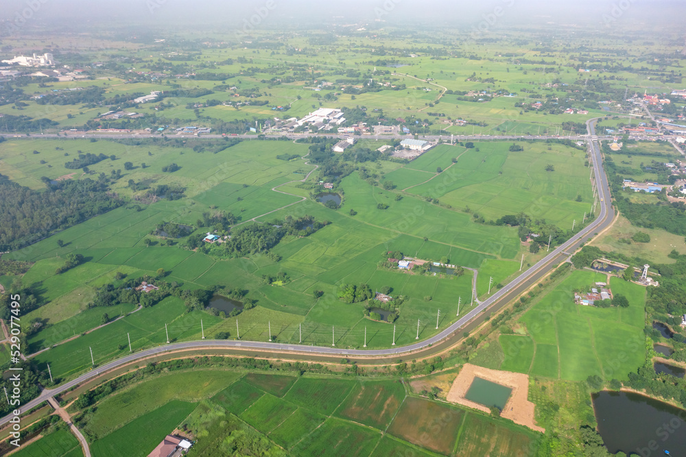 Drone view of Sufficiency Economy, Land full of agricultural activities with green rice fields, big ponds, and trees. Small houses and temple close by a pond.