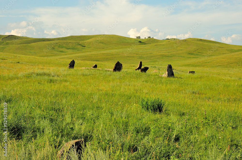 A group of ancient stone gravestones in a picturesque summer valley surrounded by high hills. A group of ancient stone gravestones in a picturesque summer valley surrounded by high hills.