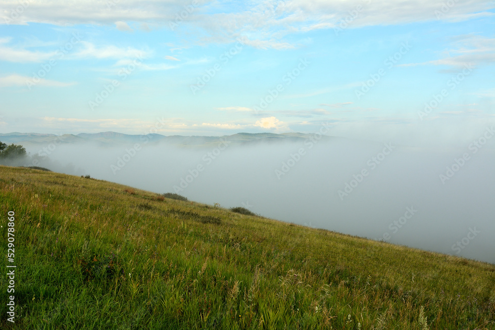 View from the top of a high hill to the valley completely hidden by dense fog.