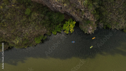 Three colorful kayaks paddling in shadow close to river shore during hot sunny day
