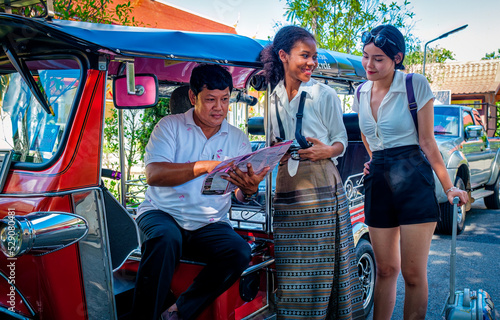 Two young European girl travelers get information and bargain the tuk tuk taxi rate for travelling around Chiang Mai downtown. Transportation concept.