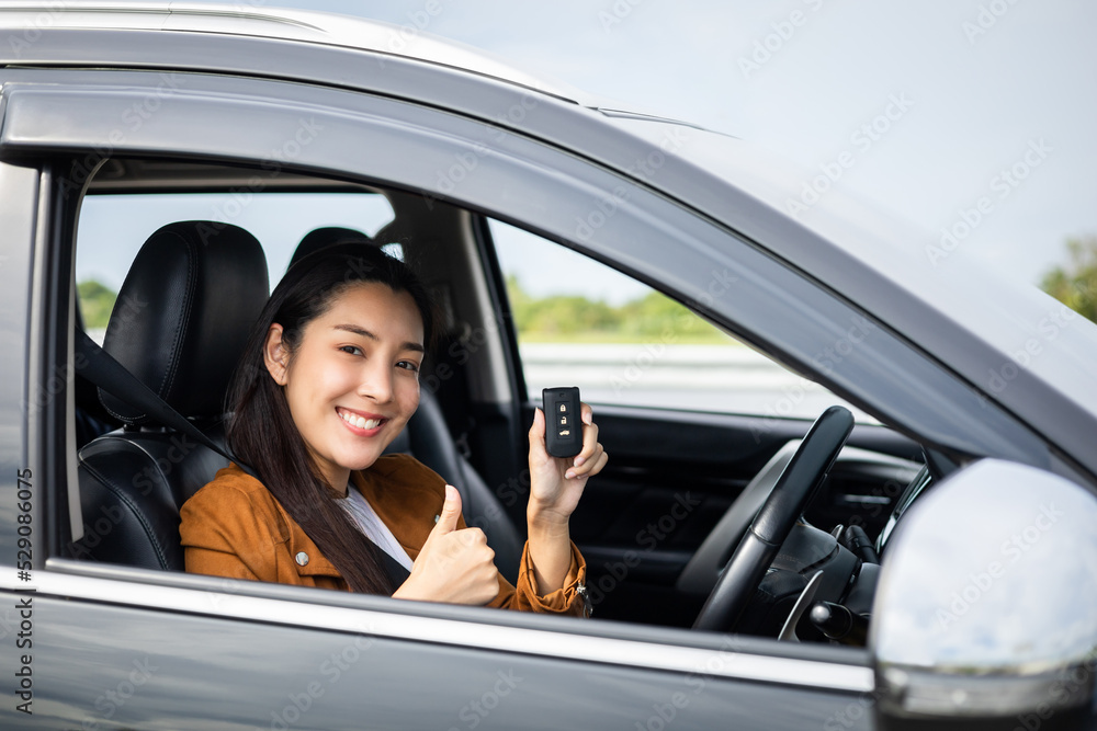 Young beautiful asian women getting new car. she very happy and excited looking outside window in hand holding car key. Smiling female driving vehicle on the road on a bright day