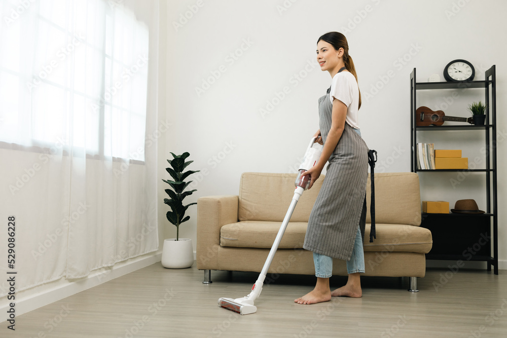 Housewife using vacuum cleaner on the floor. Wearing an apron to clean the living room at house. Young woman is happy to clean home. Maid cleaning service. Housewife using vacuum cleaner on the floor. Wearing an apron to clean the living room at house. Young woman is happy to clean home. Maid cleaning service.
