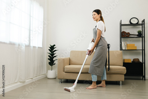 Housewife using vacuum cleaner on the floor. Wearing an apron to clean the living room at house. Young woman is happy to clean home. Maid cleaning service.
