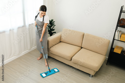 Young beautiful woman with apron and rubber glove with mop ready for cleaning home. Housekeeping housework or maid worker holding mop cleaning floor